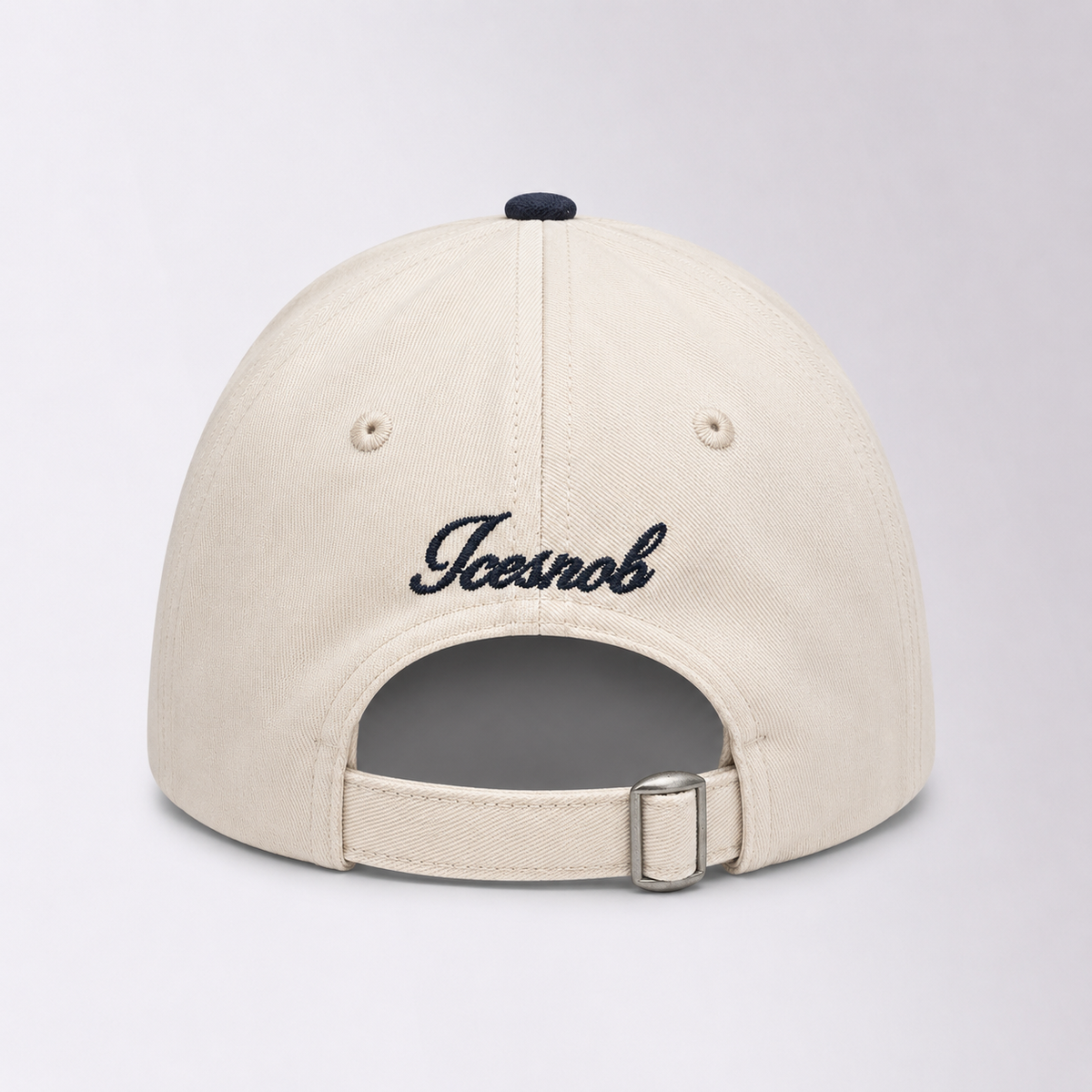 The back of a cream-colored baseball cap featuring the word 'Jeesnob' embroidered in black script across the center, with an adjustable strap and silver metal buckle at the bottom.