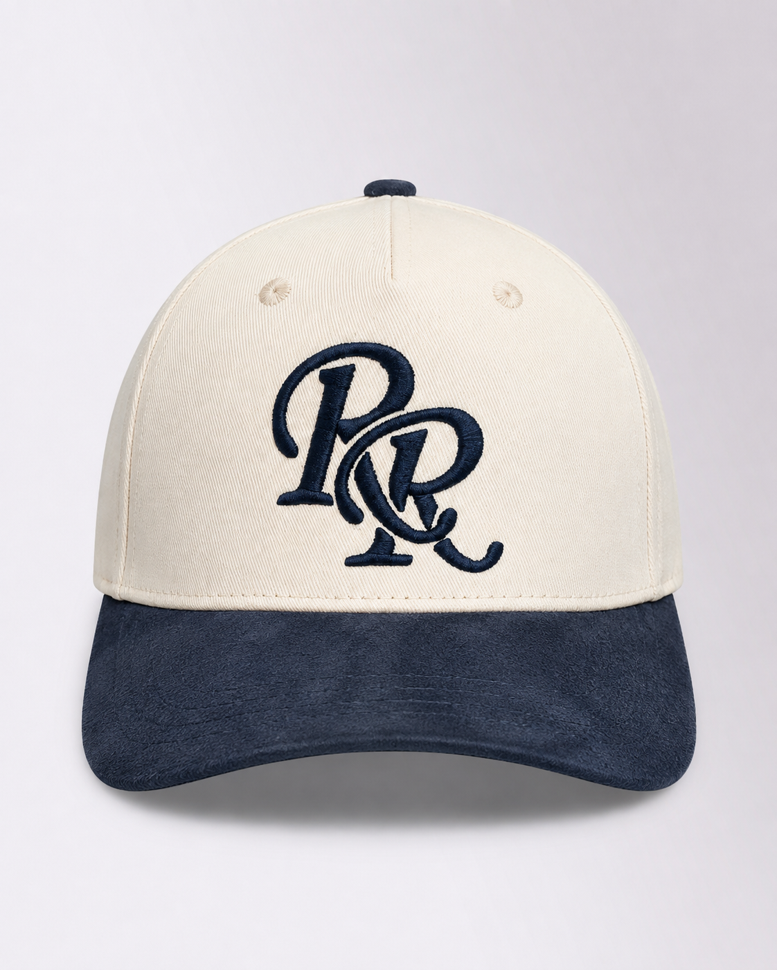 A structured baseball cap with an off-white crown and a dark navy blue brim, featuring a navy blue embroidered 'PR' monogram logo on the front. The cap is photographed against a neutral light gray background.