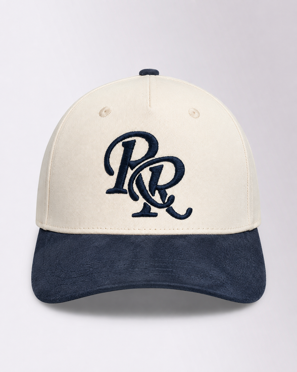 A structured baseball cap with an off-white crown and a dark navy blue brim, featuring a navy blue embroidered 'PR' monogram logo on the front. The cap is photographed against a neutral light gray background.